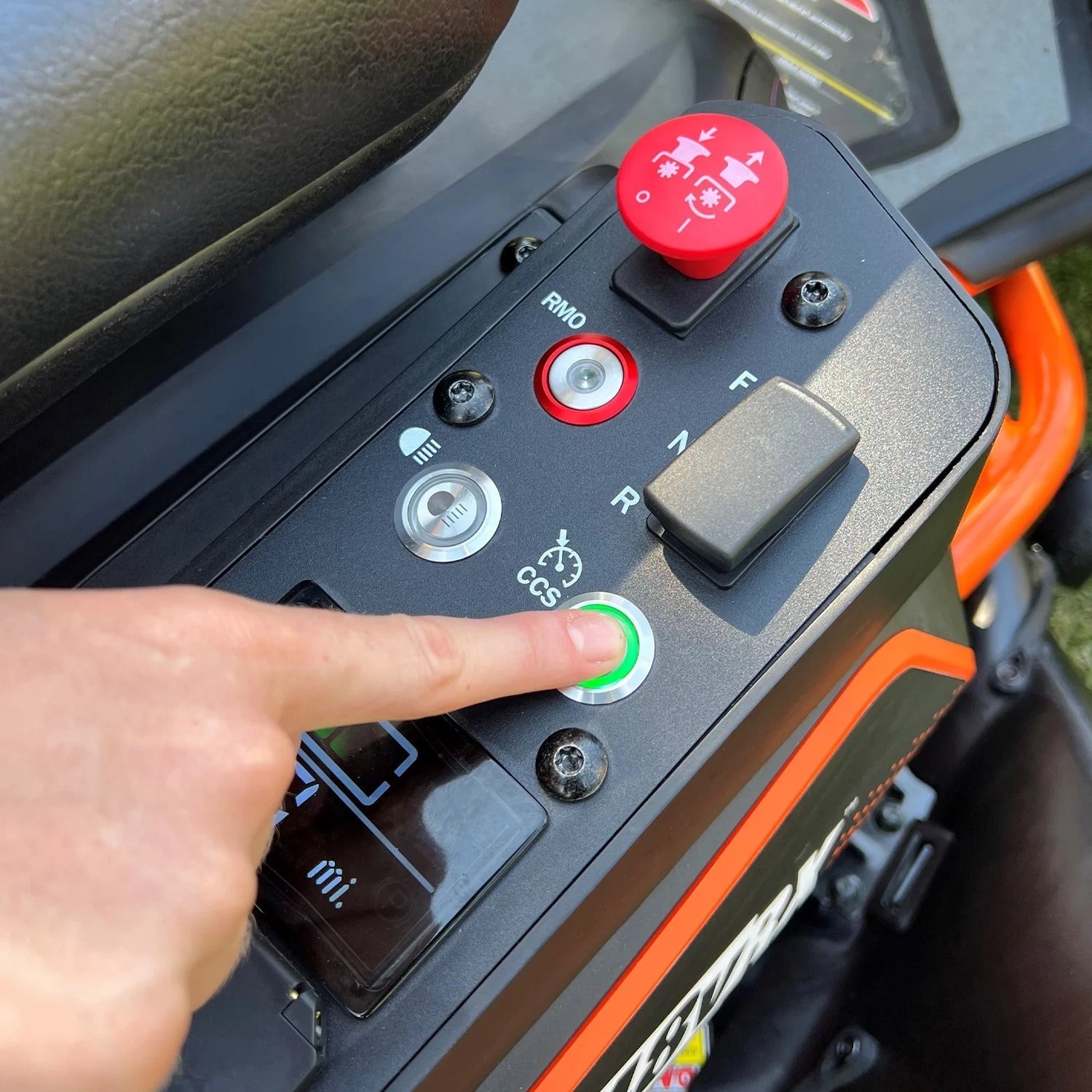 Hand pressing a green button on an electronic device with various controls and buttons.