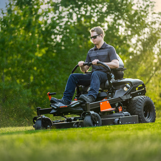 Man operating a riding lawn mower in a grassy area with trees in the background