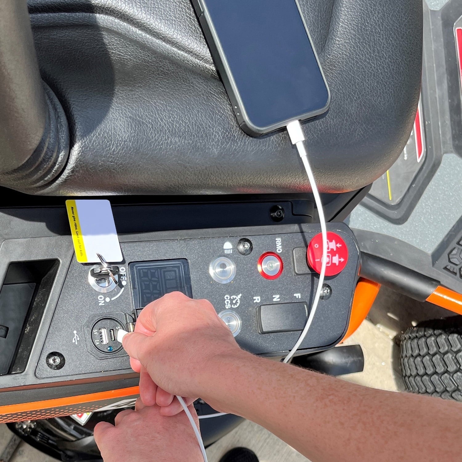 Hand plugging a device into a vehicle's power outlet with a smartphone on top.