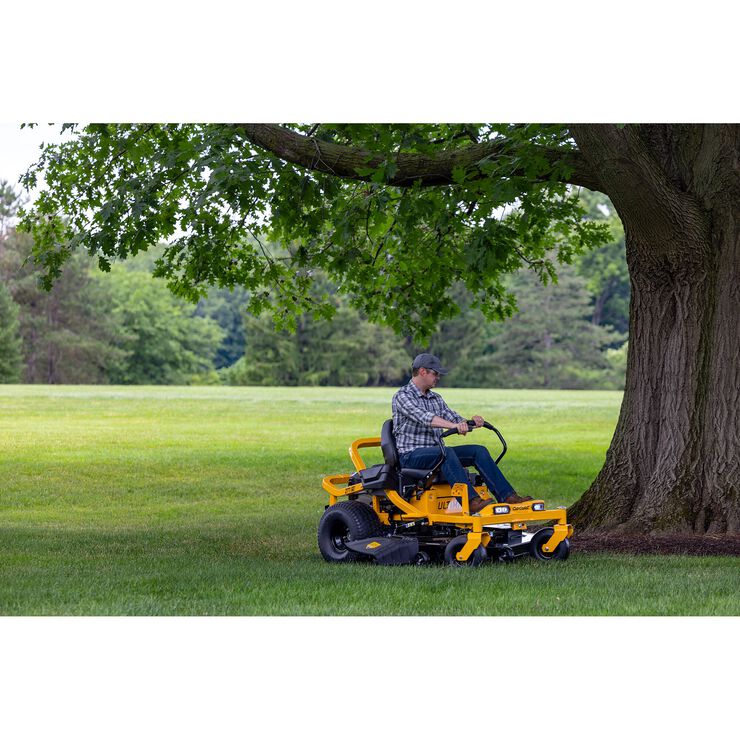 Person operating a yellow riding lawn mower in a park setting with trees and grass.