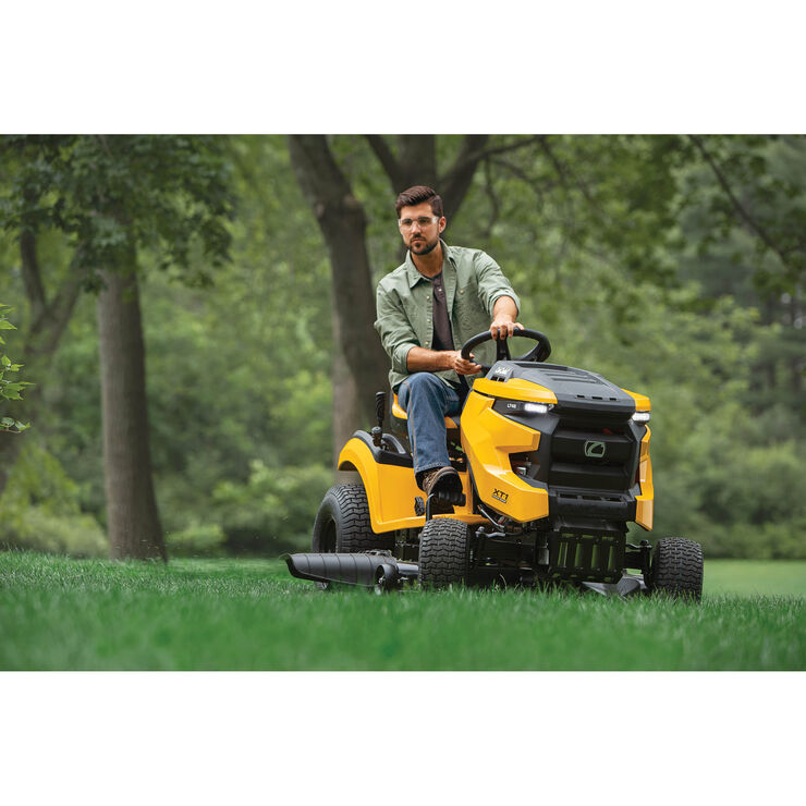 Man operating a yellow riding lawn mower in a park setting