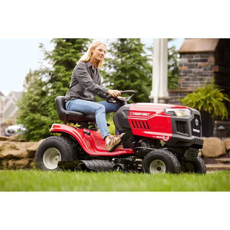 Woman operating a red riding lawn mower in a garden setting
