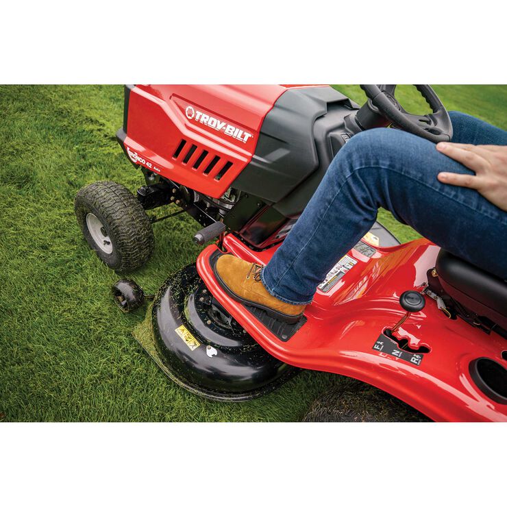 Person operating a red Troy-Bilt riding lawn mower on grass