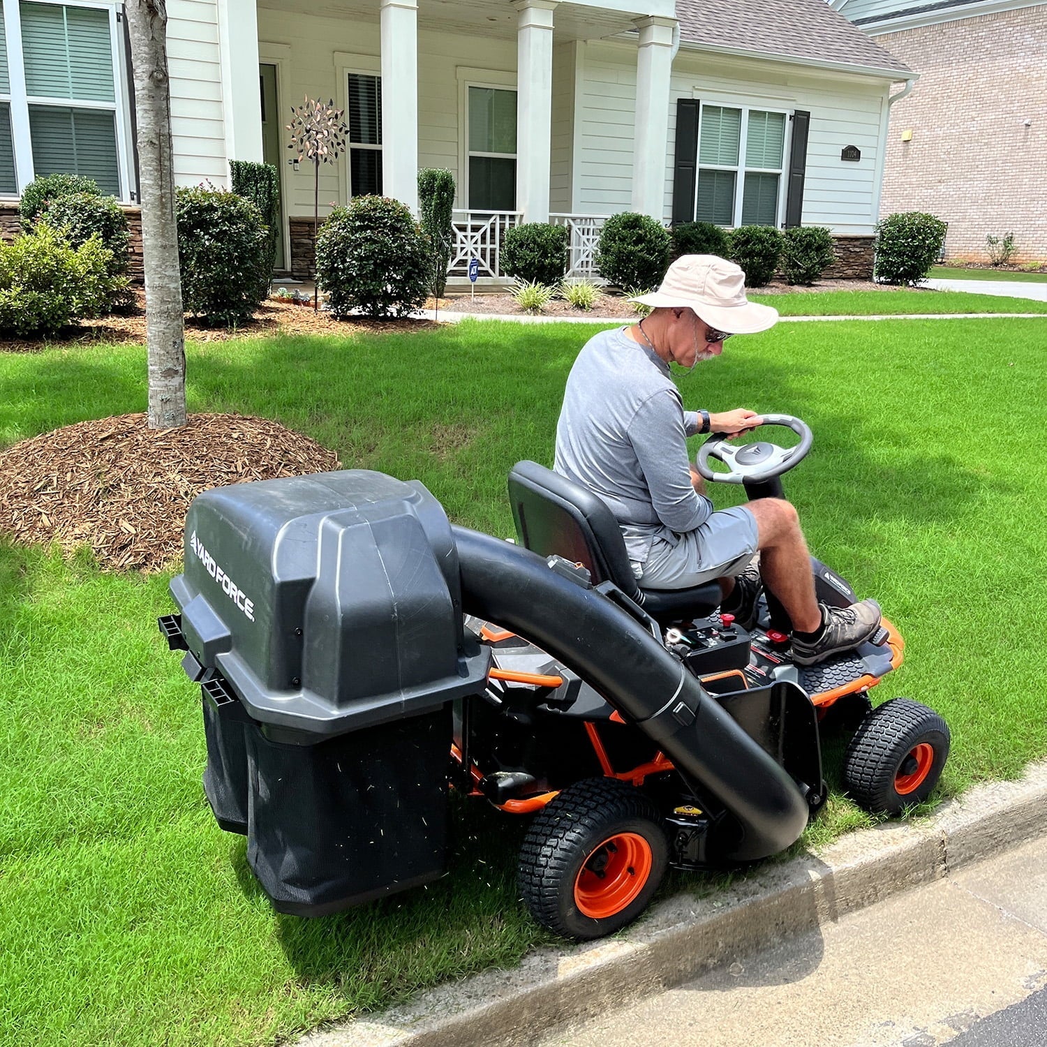 Man operating a riding lawn mower on a well-maintained lawn in front of a house.