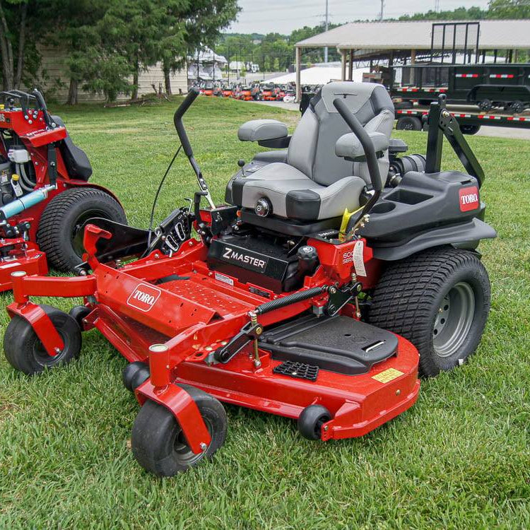 Red zero-turn lawn mower on a grassy area with additional mowers and equipment in the background.