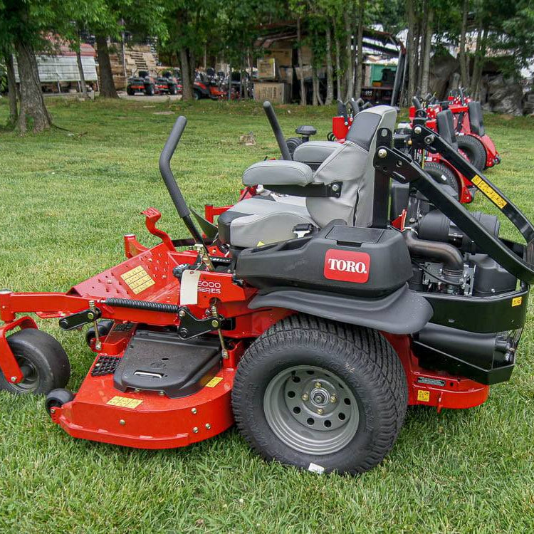  Toro lawn mower on grass with trees and equipment in the background