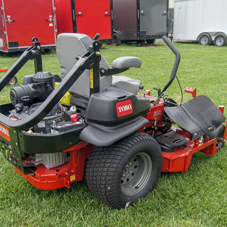 Red and black Toro lawn mower on grass with trailers in the background