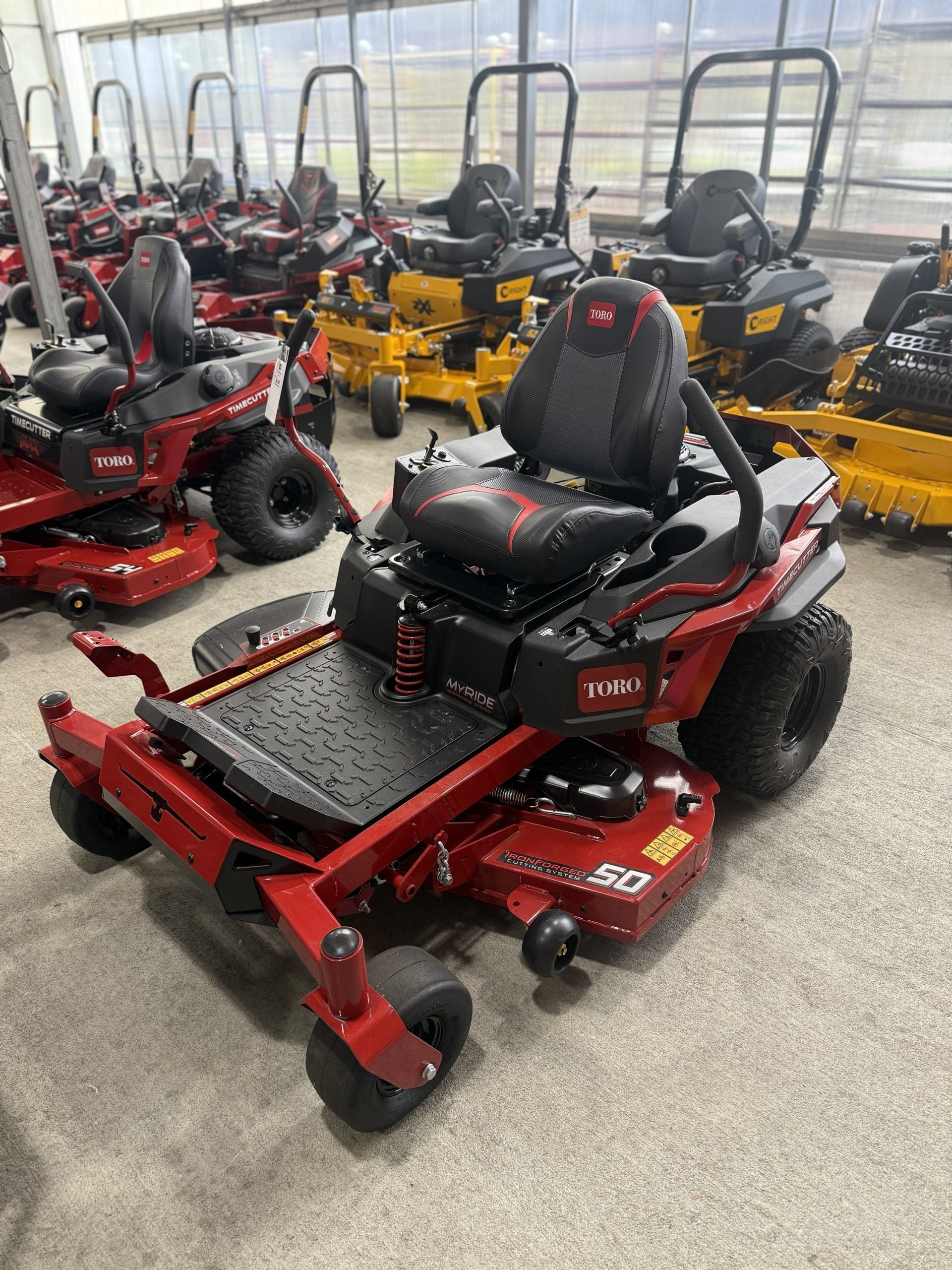 Red Toro riding lawn mower in a showroom setting with other mowers in the background.

